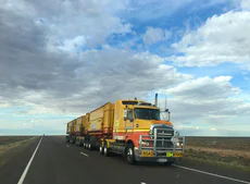 Photo of a yellow semi truck driving on a rural road.